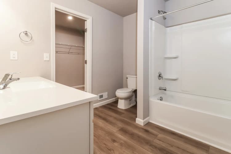 Portage apartments for rent - image - Elegant bathroom featuring a modern vanity, pristine bathtub, and chic wood flooring leading to a spacious walk-in closet.